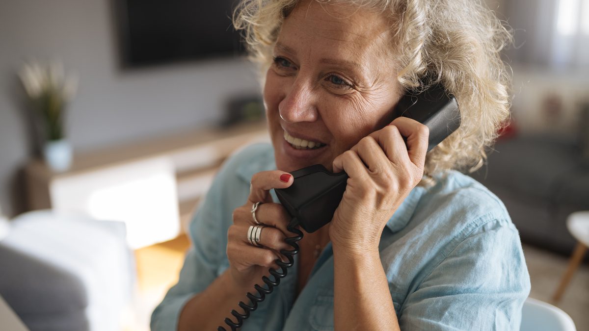 A woman smiling while talking on a landline phone at home
