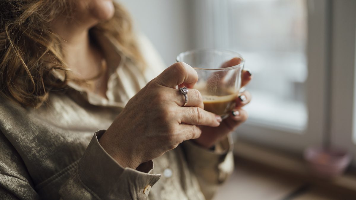 A woman holding a cup of coffee while sitting by a window