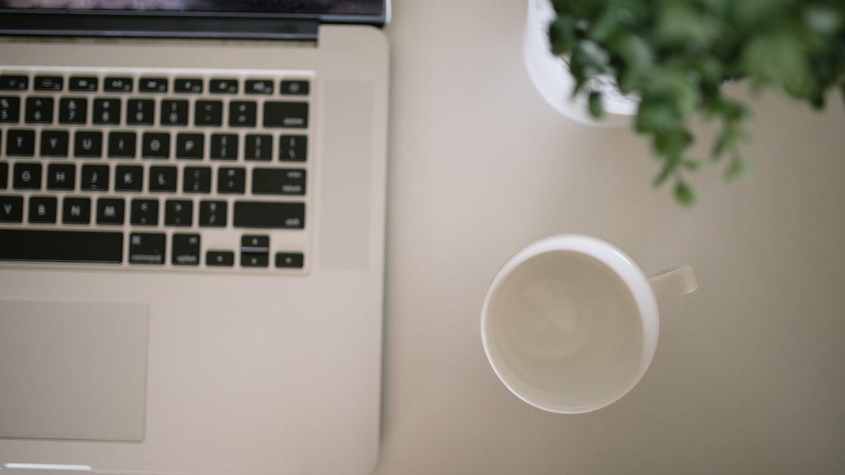 A laptop, coffee cup, and plant on a desk