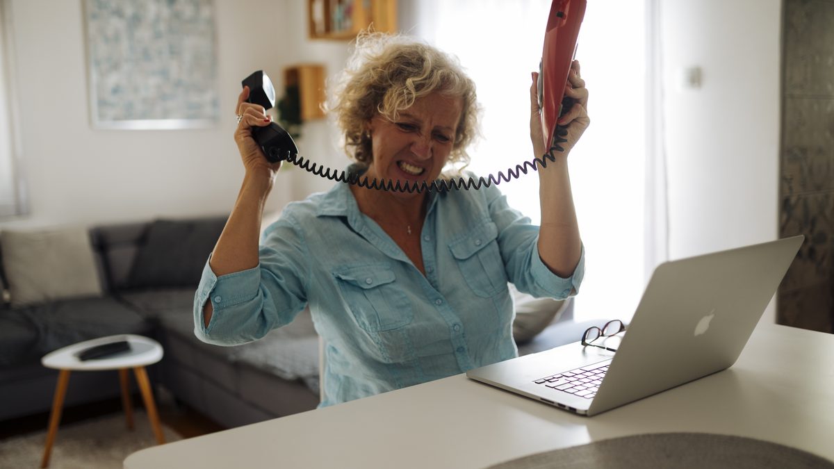 A woman holding a phone in each hand while sitting at a laptop