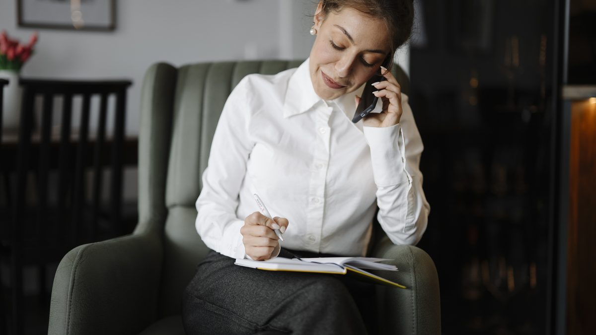 A woman talking on the phone while writing in a notebook